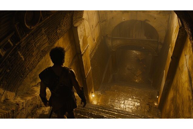 A gladiator pausing at a junction beneath an arena, one passage well-lit and orderly, the other narrow and shadowed, posture measured and undecided